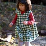 A child outside, playing in the sun and collecting sticks, wearing the Little Green Radicals Long Sleeve Waffle Top - Hazelnut underneath a green check pinafore dress