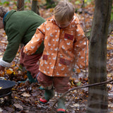 Child at a campfire in a forest wearing a Kids Warm Waterproof Winter School Coat in a gold yellow duck print, blue and floral, by Little Green Radicals, made from recycled bottles and a cosy polyester fleece, buy now at Babipur.
