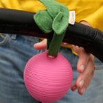 The texture of the Ramona Radish Pacifier Holder which has been tied onto a pram handle. A persons hand is reaching towards the holder.