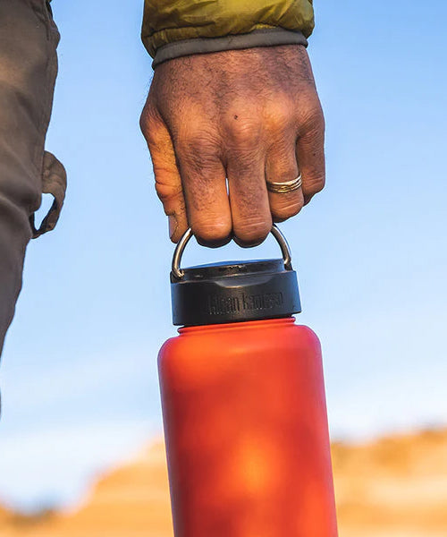 A person holding a Klean Kanteen bottle with the Klean Kanteen Wide Loop Cap - With Bale, by the carry handle