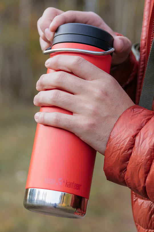 Hands holding a Klean Kanteen TKWide reusable stainless steel bottle in red with a black cap, insulated and plastic free, to represent Klean Kanteen TKWide range for sale at Babipur, official UK stockist.