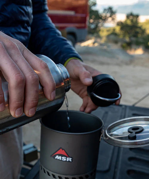 A person holding the Klean Kanteen Wide Loop Cap - With Bale, in their hand whilst pouring a drink from a Klean Kanteen