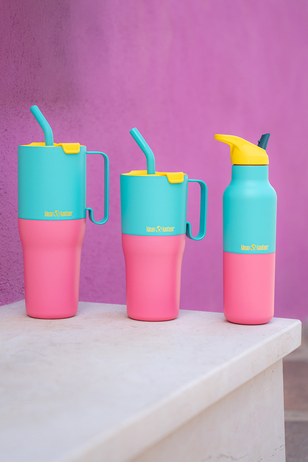 Three colorful steel  Klean Kanteen tumblers with straws and a water bottle on a white surface against a purple background. Available from Babipur 