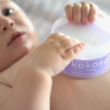 A close up of a baby holding an opened tub of Kokoso 168g baby organic coconut oil tub available at Babipur. 