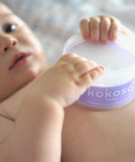 A close up of a baby holding an opened tub of Kokoso 168g baby organic coconut oil tub available at Babipur. 