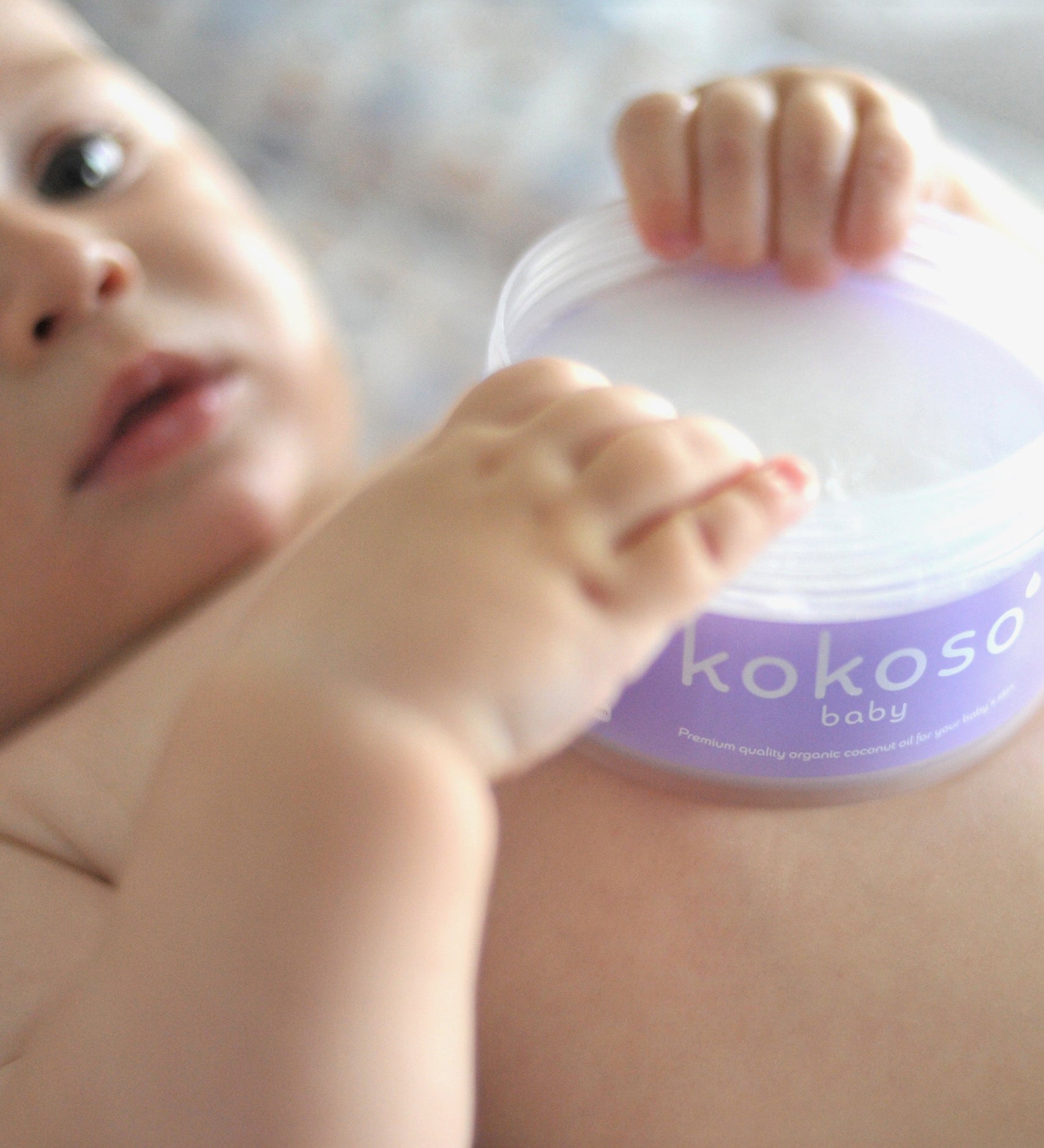 A close up of a baby holding an opened tub of Kokoso 168g baby organic coconut oil tub available at Babipur. 
