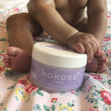 A close up of a baby holding the Kokoso 168g baby organic coconut oil tub available at Babipur. 