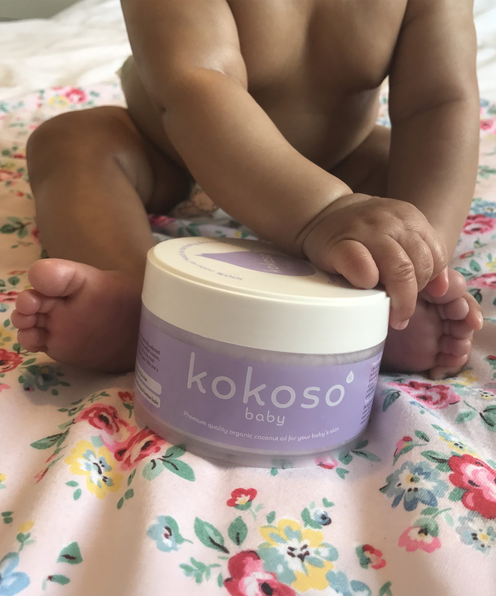 A close up of a baby holding the Kokoso 168g baby organic coconut oil tub available at Babipur. 