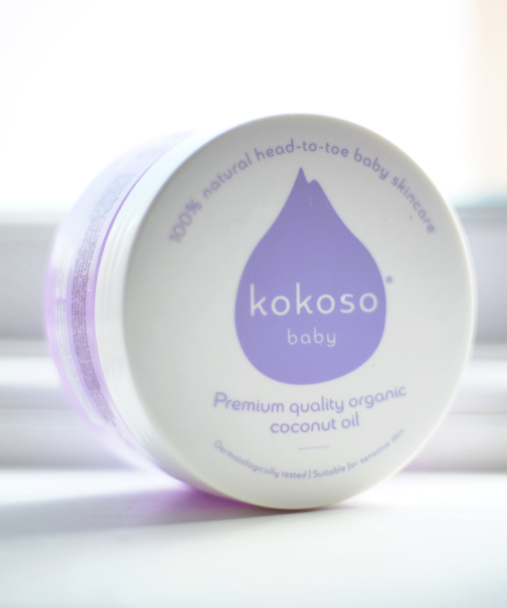 A close up of a Kokoso baby organic coconut oil tub on it's side showing the branding on the white lid. Tub available at Babipur.