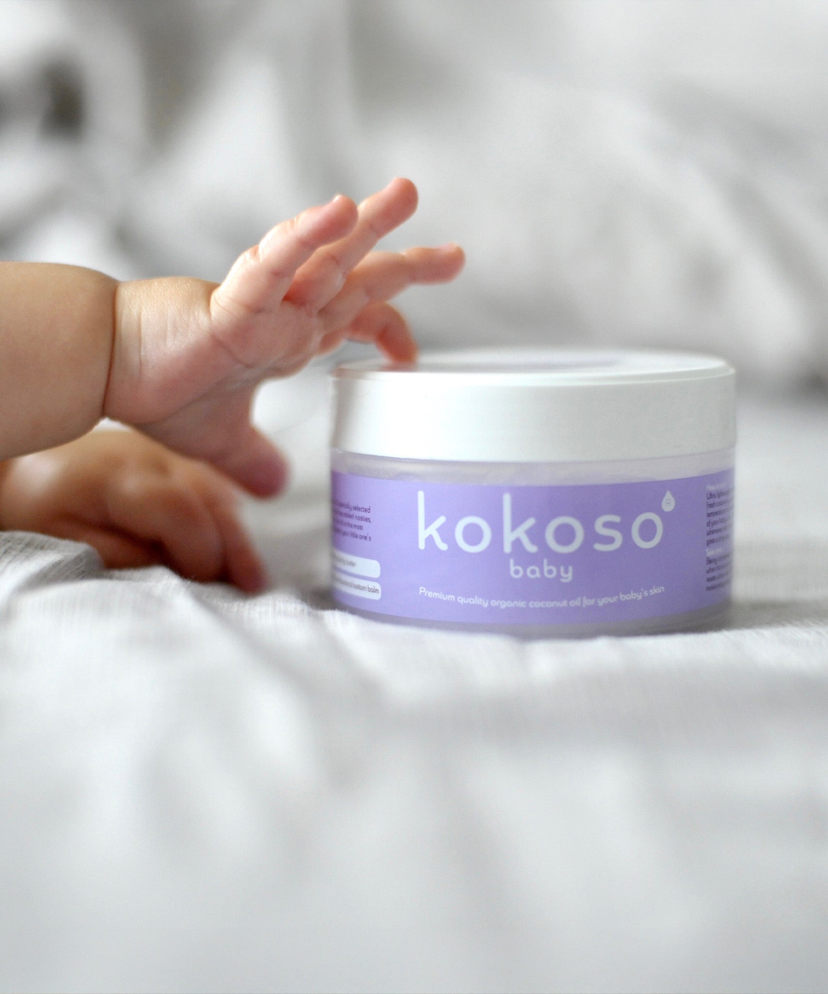 A close up of a baby's hand touching the Kokoso baby organic coconut oil, tub available at Babipur. 