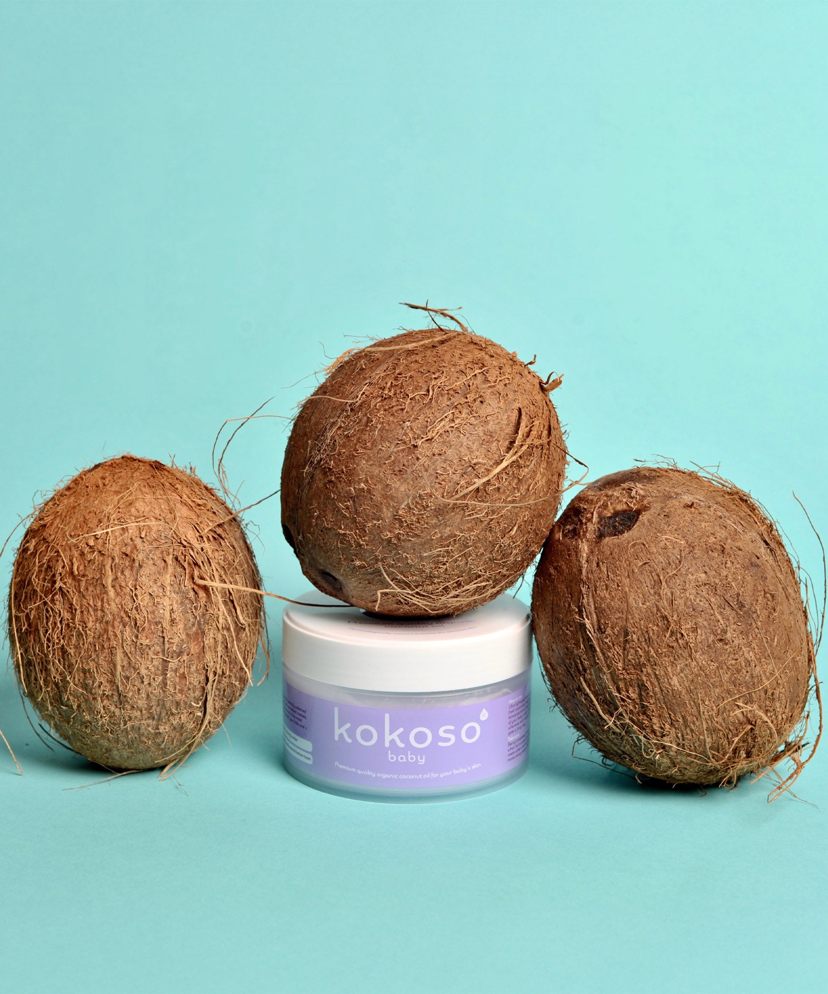 Kokoso 70g baby organic coconut oil standing next to 3 whole coconuts. Tub available at Babipur.
