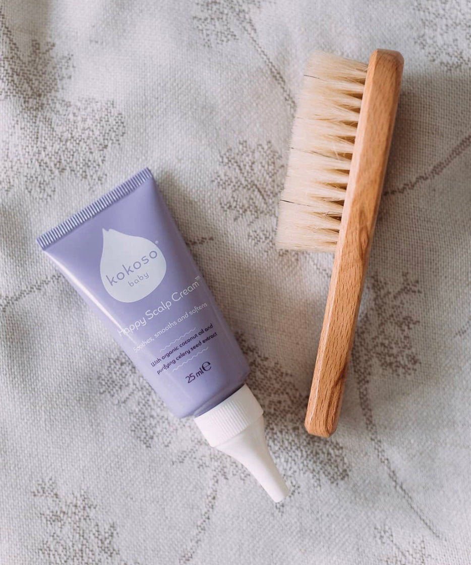 A top down image of the Kokoso Happy scalp cream next to a kokoso wooden hair brush on a soft vintage blanket available at Babipur.