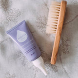 A top down image of the Kokoso Happy scalp cream next to a kokoso wooden hair brush on a soft vintage blanket available at Babipur.