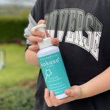 A close up of an older child holding the Kokoso protect foaming hand sanitiser 500ml bottle available at Babipur.
