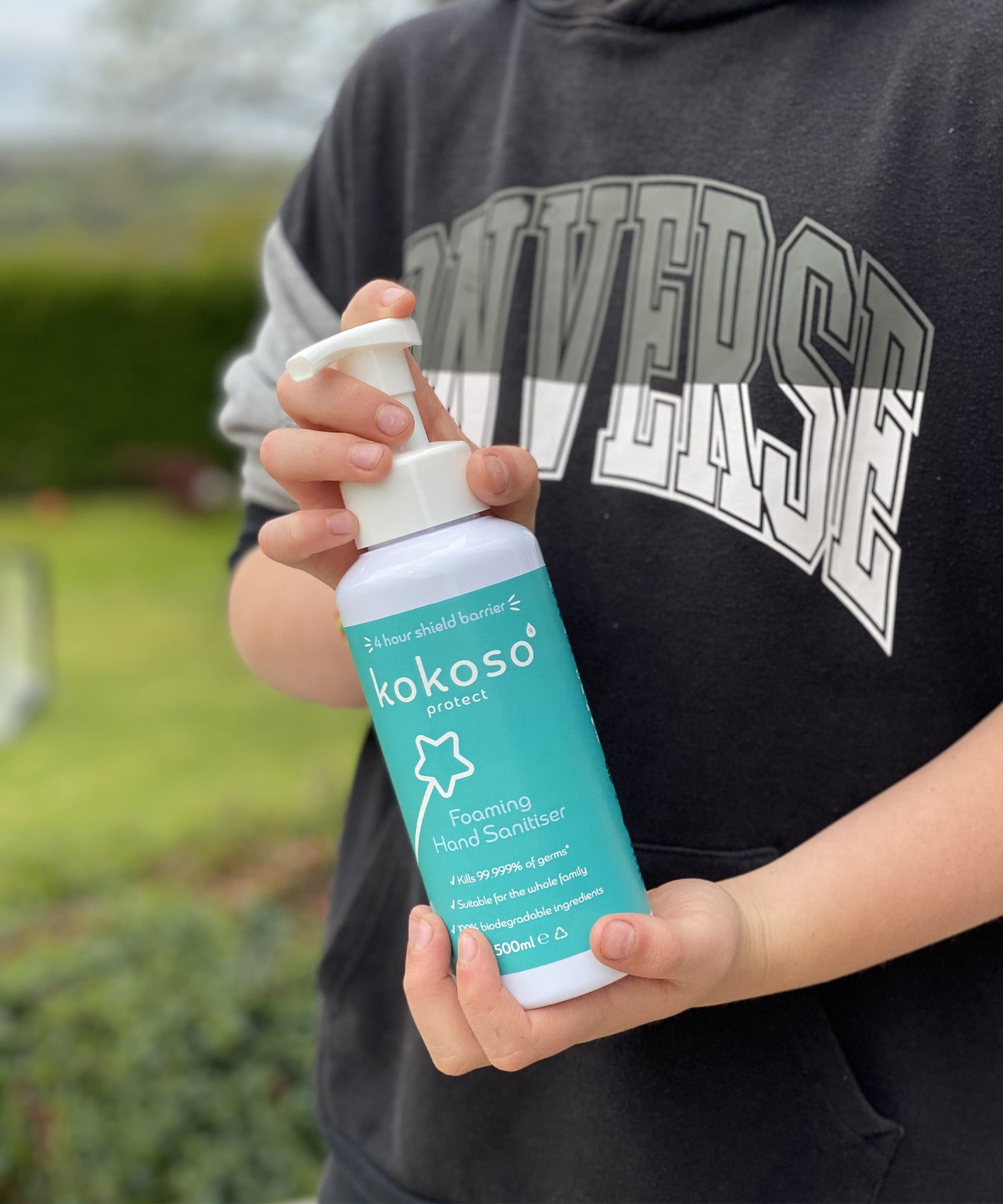 A close up of an older child holding the Kokoso protect foaming hand sanitiser 500ml bottle available at Babipur.