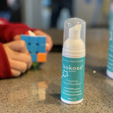 Kokoso protect foaming hand sanitiser original 50ml bottle available at Babipur on a stone surface with a child playing a puzzle game in the background.