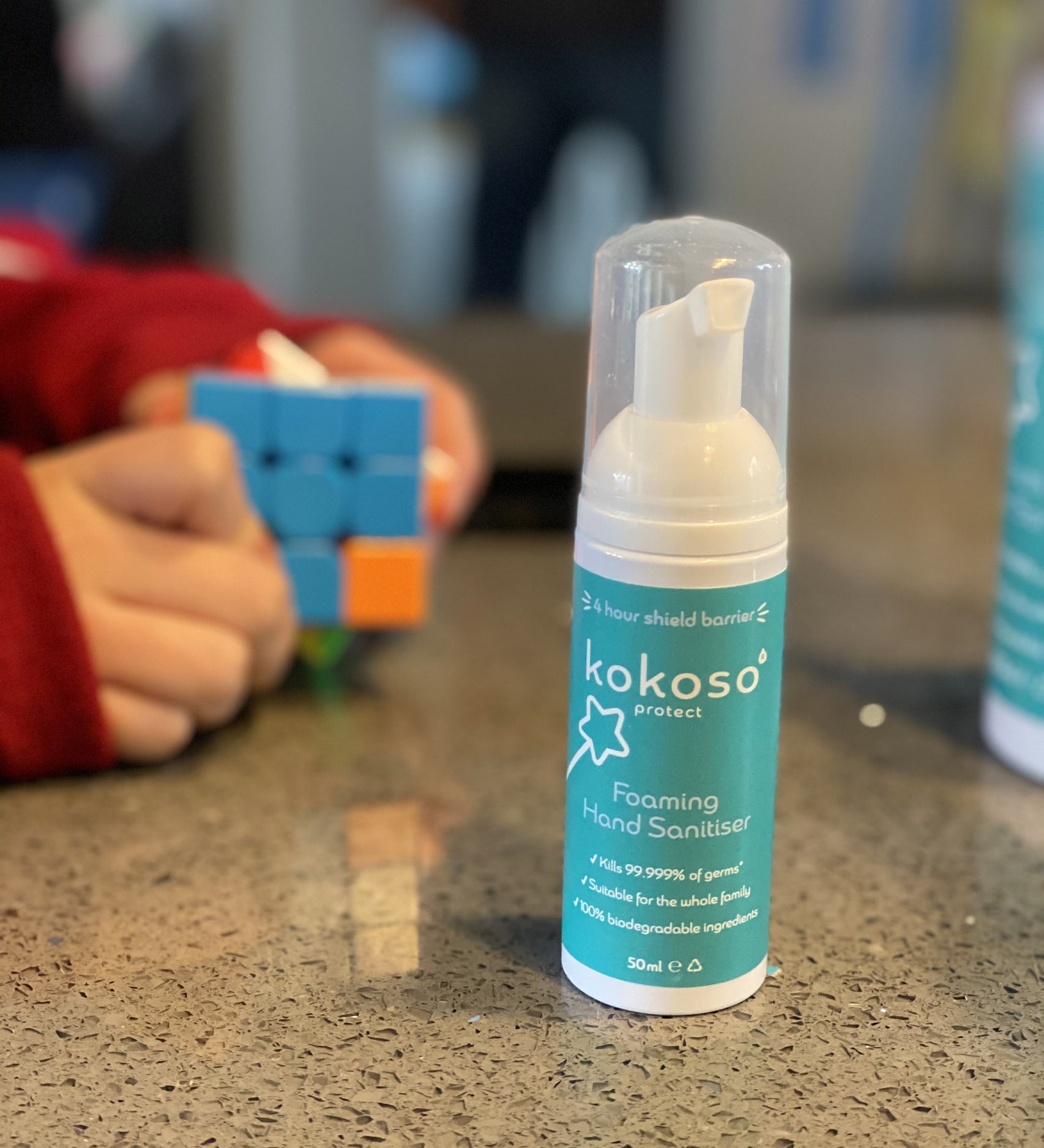 Kokoso protect foaming hand sanitiser original 50ml bottle available at Babipur on a stone surface with a child playing a puzzle game in the background.