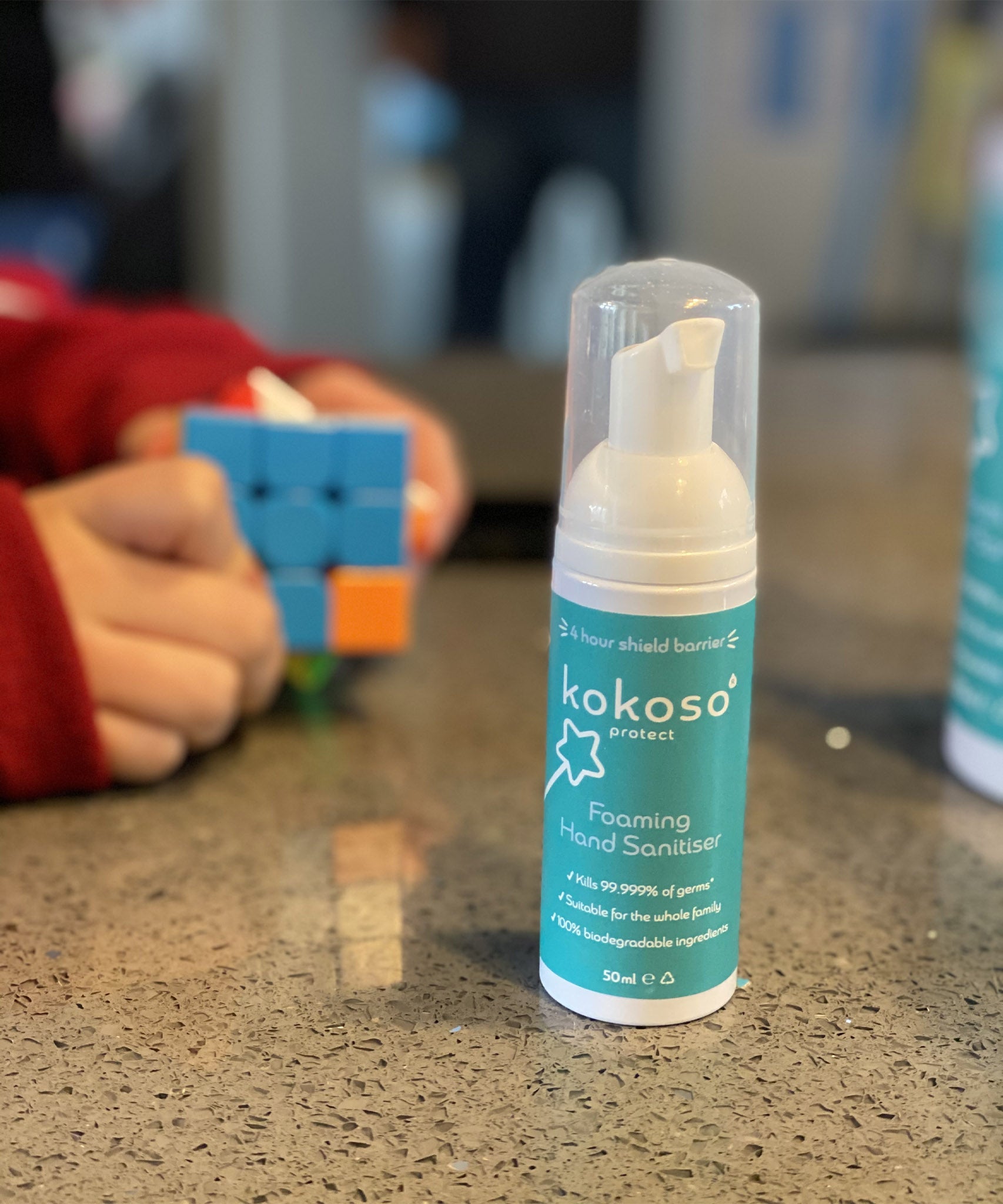 Kokoso protect foaming hand sanitiser original 50ml bottle available at Babipur on a stone surface with a child playing a puzzle game in the background.