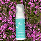 A Kokoso protect foaming hand sanitiser original 50ml bottle lying on a bed of bright pink flowers. Bottle available at Babipur.