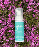 A Kokoso protect foaming hand sanitiser original 50ml bottle lying on a bed of bright pink flowers. Bottle available at Babipur.