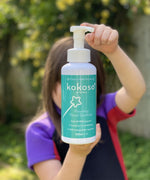 A child standing in a garden and holding the Kokoso protect foaming hand sanitiser original 500ml bottle available at Babipur.