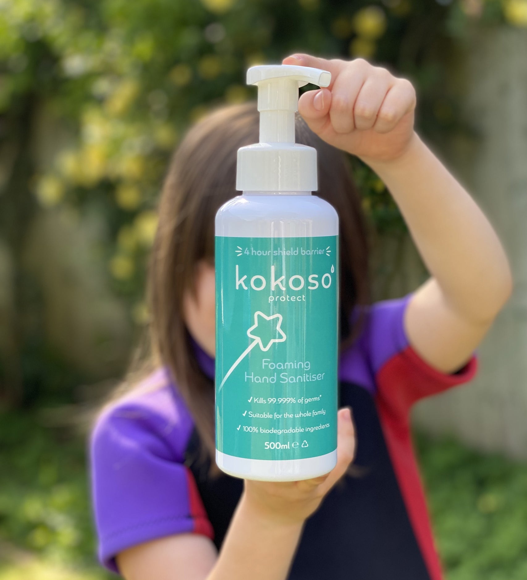A child standing in a garden and holding the Kokoso protect foaming hand sanitiser original 500ml bottle available at Babipur.