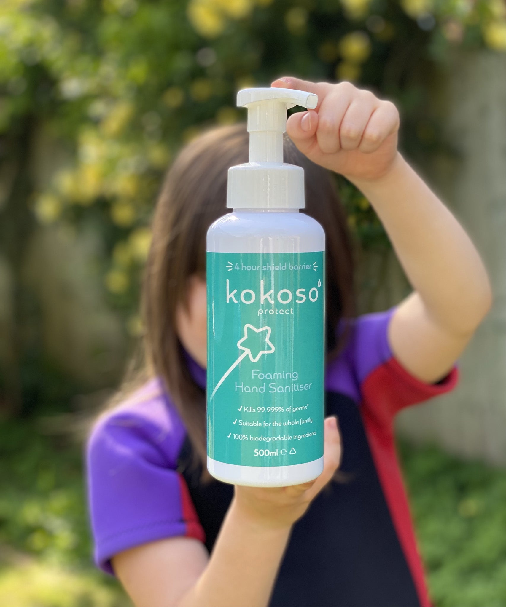 A child standing in a garden and holding the Kokoso protect foaming hand sanitiser original 500ml bottle available at Babipur.