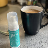 Kokoso protect foaming hand sanitiser original 50ml bottle standing next to mug of tea. Bottle available at Babipur.