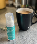 Kokoso protect foaming hand sanitiser original 50ml bottle standing next to mug of tea. Bottle available at Babipur.