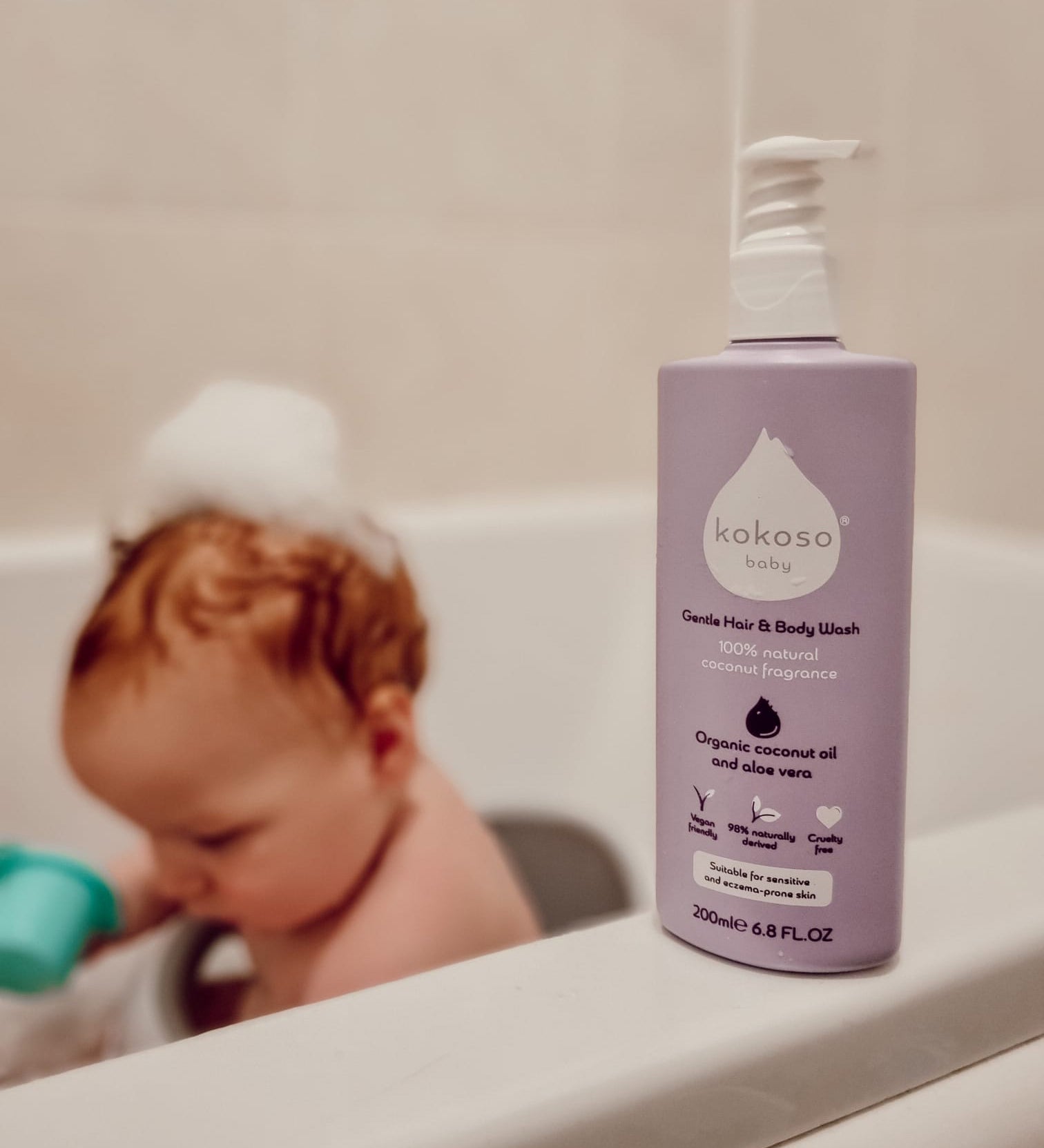 Kokoso softly coconut scented organic baby body and hair wash 200ml bottle standing on the side of the bath with a baby inside. 