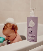Kokoso softly coconut scented organic baby body and hair wash 200ml bottle standing on the side of the bath with a baby inside. 