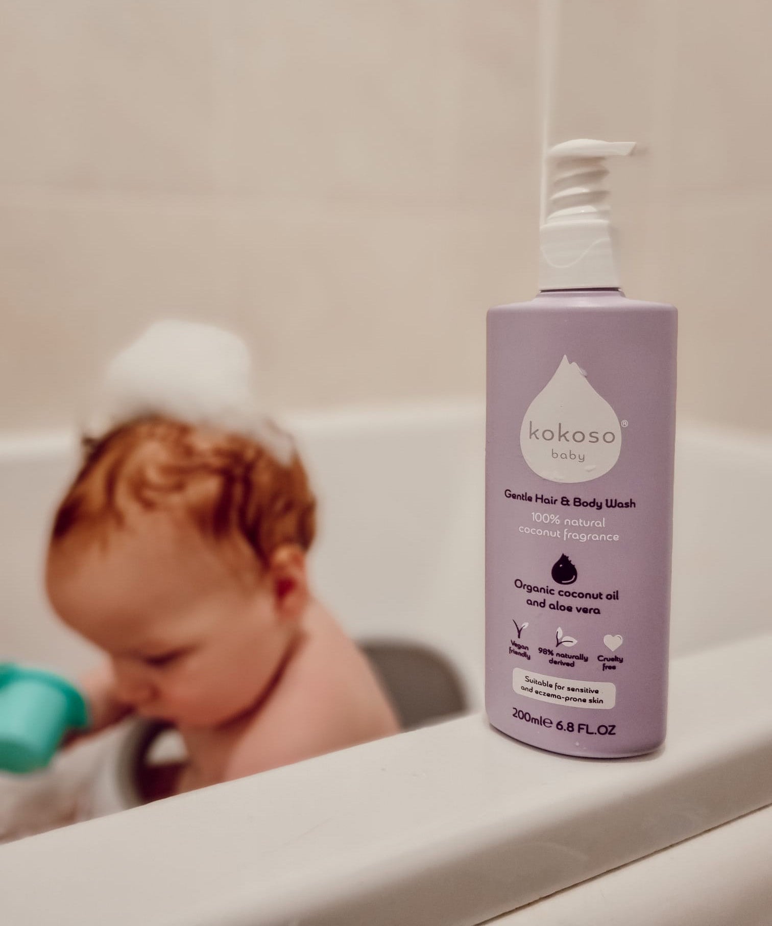 Kokoso softly coconut scented organic baby body and hair wash 200ml bottle standing on the side of the bath with a baby inside. 