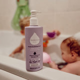 Kokoso softly coconut scented organic baby body and hair wash 200ml bottle standing on the side of the bath with a baby inside. Bottle Available at Babipur.