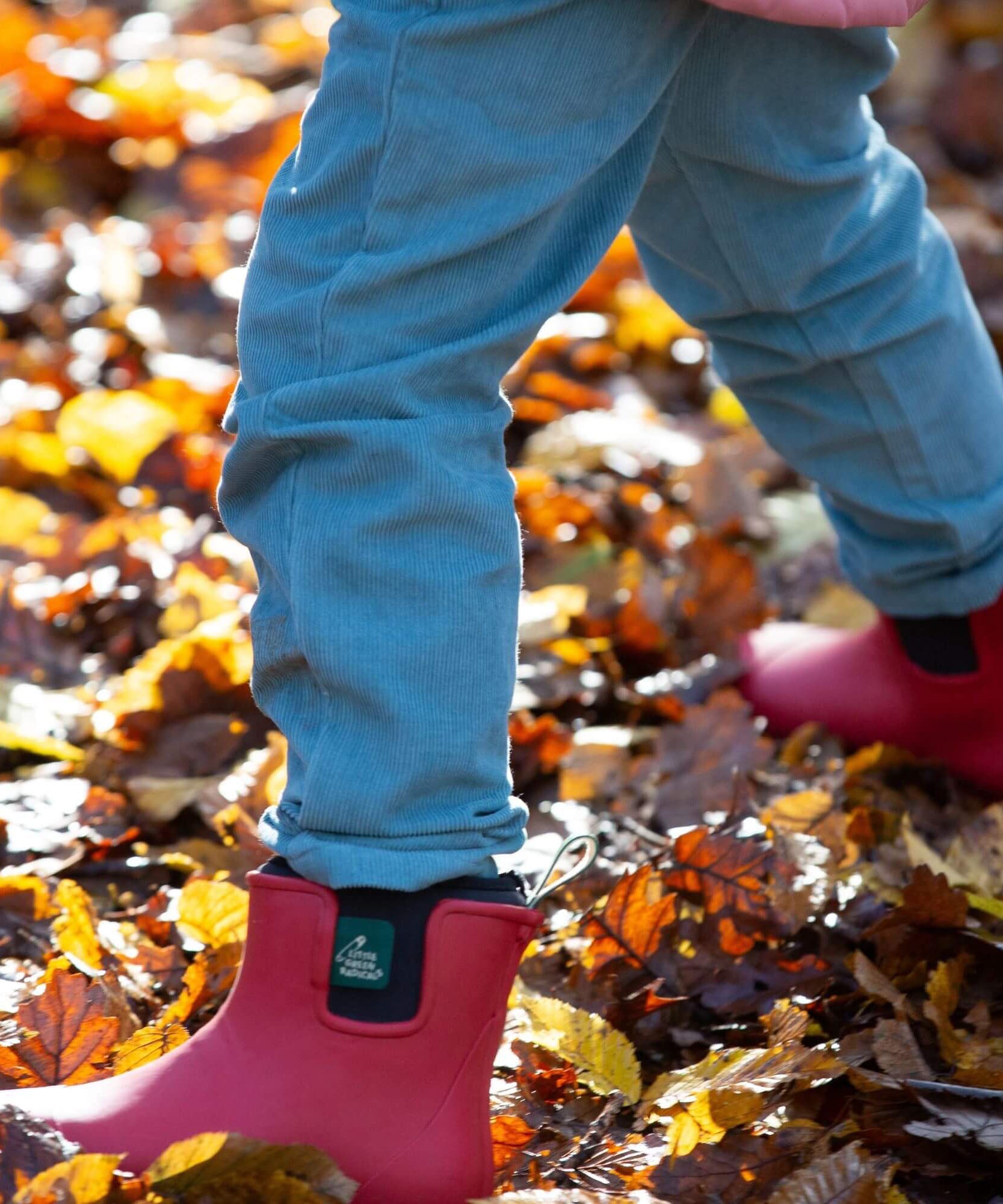 A child playing on wet leaves and wearing the Little Green Radicals natural rubber ankle wellington boots