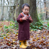 A child standing on leaves with trees in background and wearing the Little Green Radicals collecting flowers knitted collar dress.