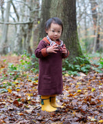 A child standing on leaves with trees in background and wearing the Little Green Radicals collecting flowers knitted collar dress.