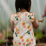 Child wearing Little Green Radicals kids flora frill summer romper dress floral design showing button fastener on upper back