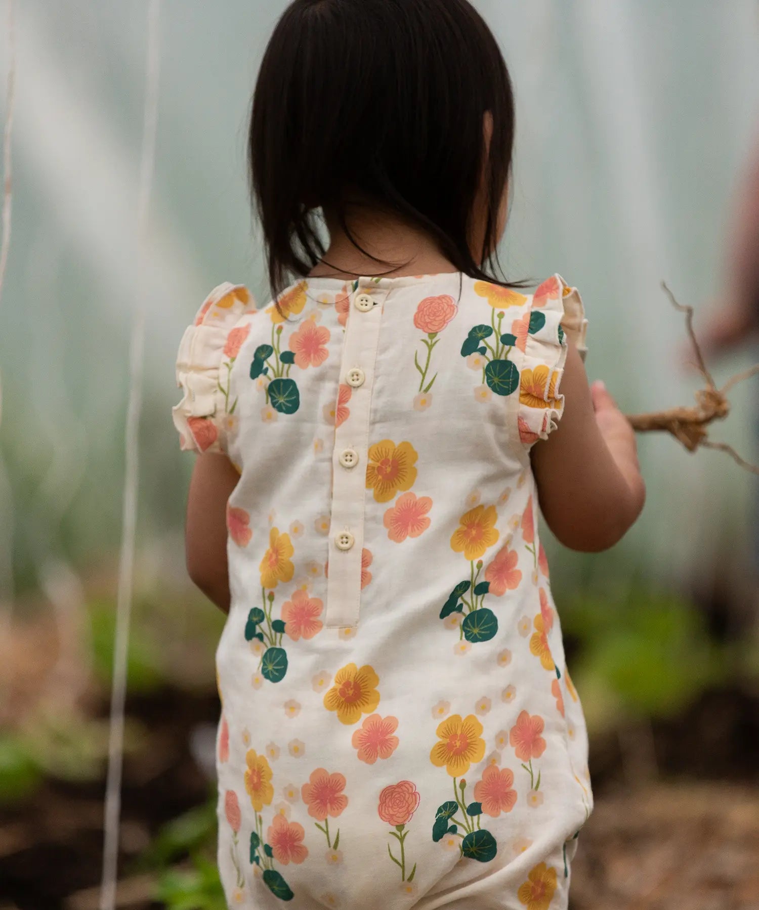 Child wearing Little Green Radicals kids flora frill summer romper dress floral design showing button fastener on upper back