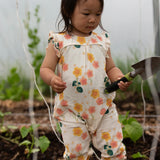 Small child wearing Little Green Radicals kids flora frill summer romper dress in cream with a repeating floral design in a garden
