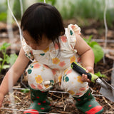 Child wearing Little Green Radicals kids flora frill summer romper dress in cream with a repeating floral design showing frill on shoulder