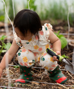 Child wearing Little Green Radicals kids flora frill summer romper dress in cream with a repeating floral design showing frill on shoulder