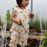 Child wearing Little Green Radicals kids flora frill summer romper dress in cream with a repeating floral design while gardening