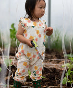 Child wearing Little Green Radicals kids flora frill summer romper dress in cream with a repeating floral design while gardening