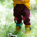 A close up of a child standing in grass and wearing the Little Green Radicals knee patch joggers showing the toadstool knee patch applique detail and the light blue and yellow cuff trim.