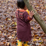 A close up of a child wearing the Little Green Radicals collecting flowers knitted collar dress showing the button fastener light brown collar detail.