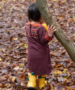 A close up of a child wearing the Little Green Radicals collecting flowers knitted collar dress showing the button fastener light brown collar detail.