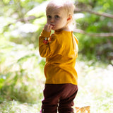 A child standing in grass and wearing the Little Green Radicals knee patch joggers in toadstool design