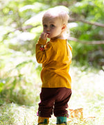 A child standing in grass and wearing the Little Green Radicals knee patch joggers in toadstool design