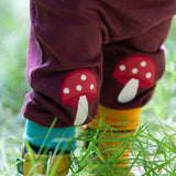 A close up of a child wearing the dark maroon Little Green Radicals knee patch joggers showing the toadstool knee patch applique detail