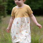 A child playing in a grassy field wearing the LGR Rainbow Balloons Easy Peasy Summer Dress